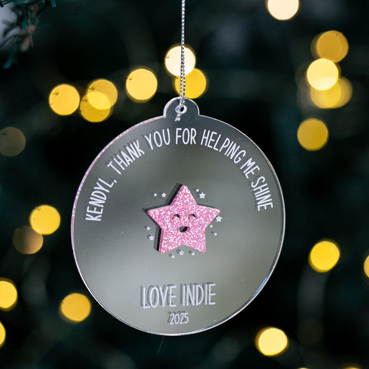 Decorative Christmas Teacher Bauble with a pink star with a face cut out, and text on a blurred light background
