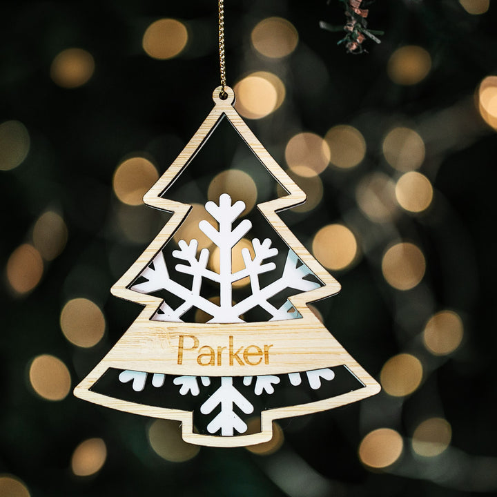 A personalized Frosted Forest Christmas Bauble with a white acrylic snowflake base and a bamboo Christmas tree cut out with the name &