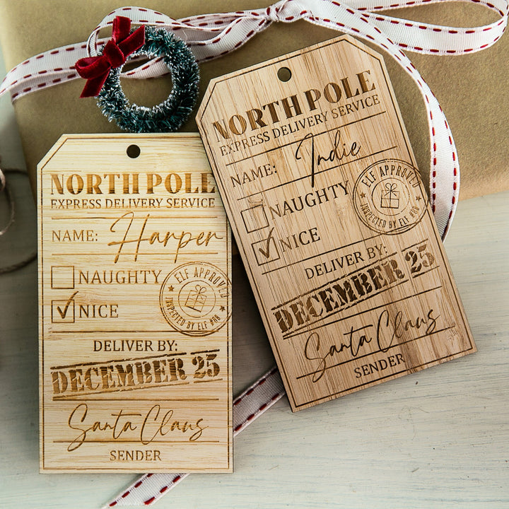 Personalised North Pole Gift Tag features "North Pole Express Delivery Service" text, "Naughty" and "Nice" checkboxes marked "Nice", custom names, Santa’s signature, plus ribbon and wreath accents.