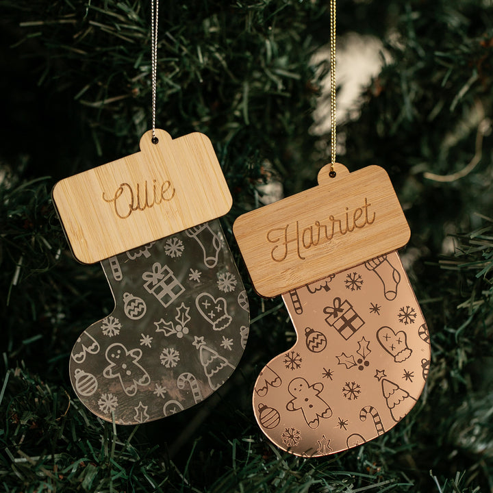 Two Christmas Stocking Baubles with holiday-themed engravings hang on a tree, each personalised with names like Ollie and Harriet. These festive ornaments make perfect custom decorations for your Christmas celebrations.