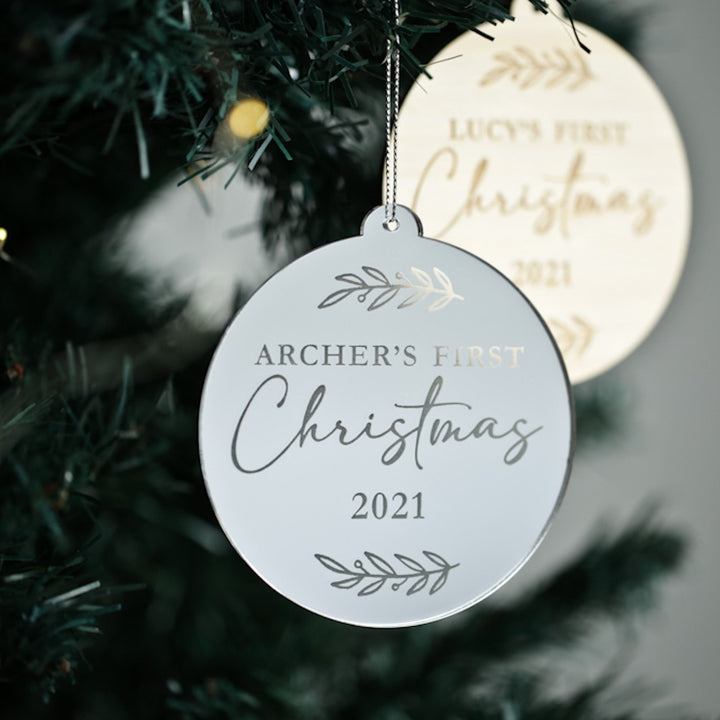 A close-up of the First Christmas Laurel Christmas Bauble reads Archer’s First Christmas 2021, with a gold ornament in the background—a perfect keepsake gift for celebrating baby’s first holiday season.