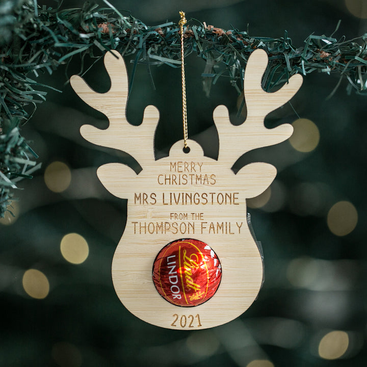 A wooden reindeer-shaped Christmas ornament with a hanging ribbon, featuring a &