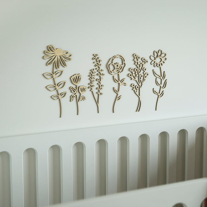 The Secret Garden Stems Set, featuring wooden floral wall decor, is mounted above a white crib with rounded slats for a minimalist and modern nursery wall installation.