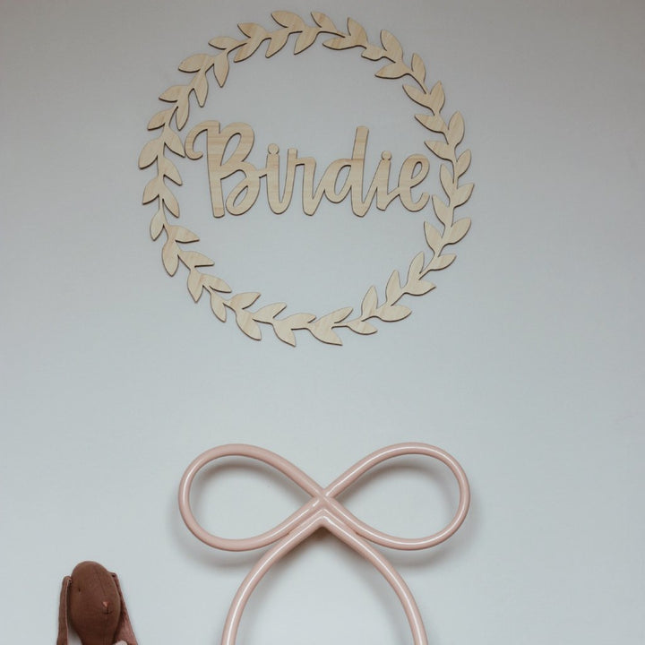 A leafy-look bamboo wreath, surrounding a bamboo personalised wall name saying Birdie. Hanging in a child&