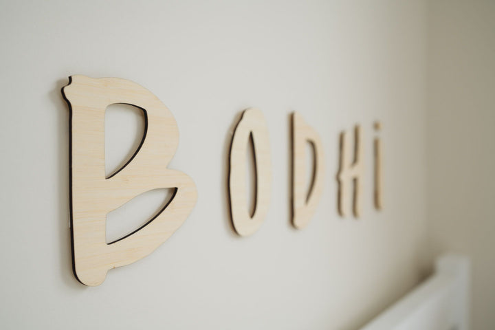 A bamboo hand lettered wall name saying Bodhi, hanging above a bed.
