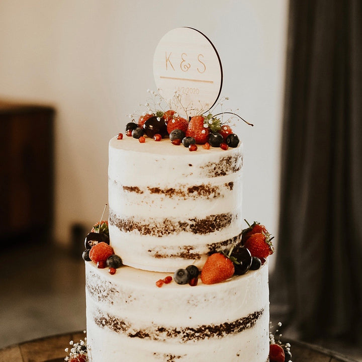 A two-tiered naked cake with fresh strawberries, blueberries, and red berries is topped with the Together Cake Topper (available in two colours) and displayed on a rustic wooden table.