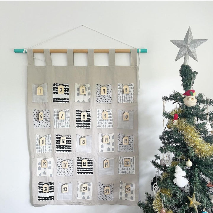 The Advent Calendar Tags Set displayed on a fabric advent calendar with numbered pockets, hanging beside a decorated Christmas tree.