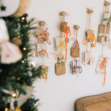 A decorated Christmas tree stands in front of a wall display featuring small gift boxes and bags hung on strings, each labelled with the Advent Calendar Tags Set and tied with ribbons.