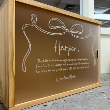 The Personalised Christmas Keepsakes Memory Boxes feature a wooden design, a frosted sliding lid with a white bow illustration, and can be customised with a heartfelt message like: “Harper, This little box I give to you... With love, Mum x.”.
