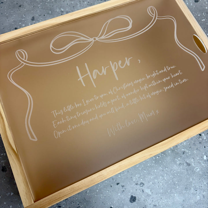 A Personalised Christmas Keepsakes Memory Box with a translucent cover, white bow illustration, and a heartfelt message to Harper in elegant script, beautifully displayed on a gray speckled surface.