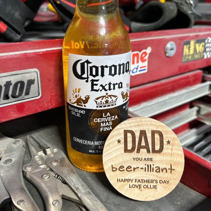 A bottle of Corona Extra sits on a red toolbox next to pliers and a Personalised Magnetic Bottle Opener (3 designs available). A wooden coaster reads: DAD YOU ARE beer-illiant. HAPPY FATHERS DAY LOVE OLLIE—a perfect personalised gift for men.