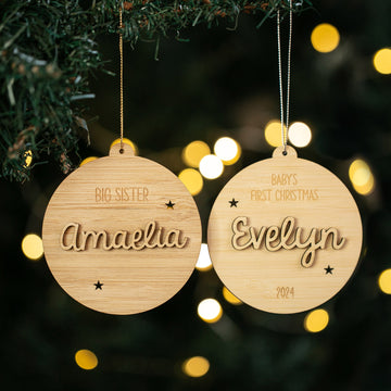 Two Celebration Christmas Baubles hang on a tree—one reads Big Sister Amaelia and the other Baby&