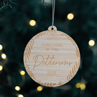 Wooden Christmas ornament with 'Christmas at the Pettersons 2025' text, hanging on a tree with lights.