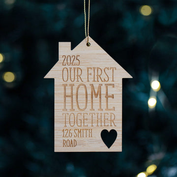 House-shaped wooden ornament with engraved text hanging on a Christmas tree.