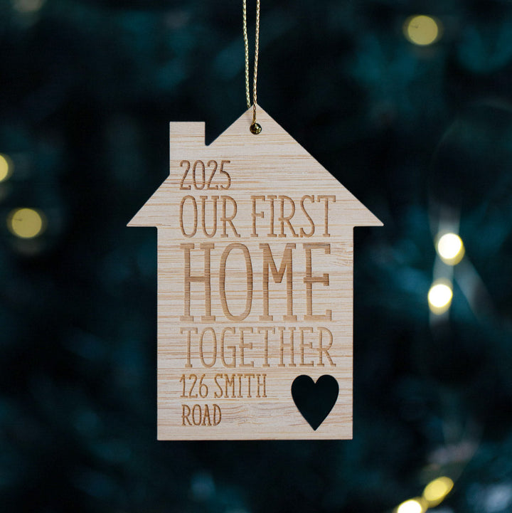 House-shaped wooden ornament with engraved text hanging on a Christmas tree.