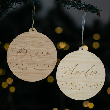 Two wooden ornaments with engraved names against a dark background with bokeh lights