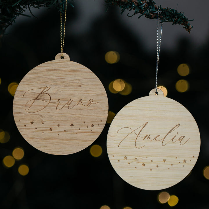Two wooden ornaments with engraved names against a dark background with bokeh lights