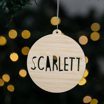 Wooden ornament with 'SCARLETT' text against a blurred festive background