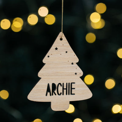 Wooden Christmas tree ornament with 'ARCHIE' on a blurred lights background