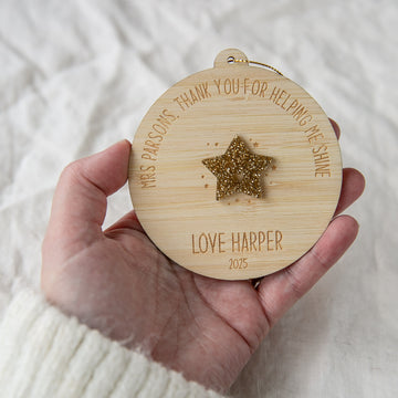 Wooden ornament with engraved text and star, held in a hand against a white background