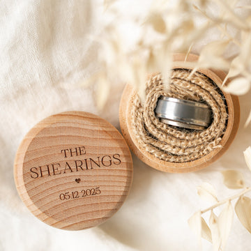A Personalised Ring Box engraved with THE SHEARINGS 05.12.2025 on the lid, featuring two rings in twine, surrounded by dried flowers and light fabric.