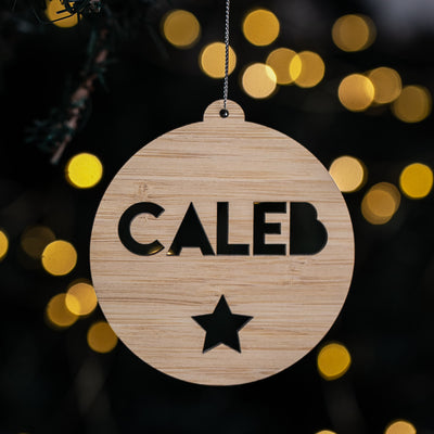 Wooden ornament with 'CALEB' and a star cutout against a blurred light background