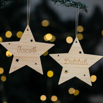 Two wooden star ornaments with engraved names against a festive background with lights.