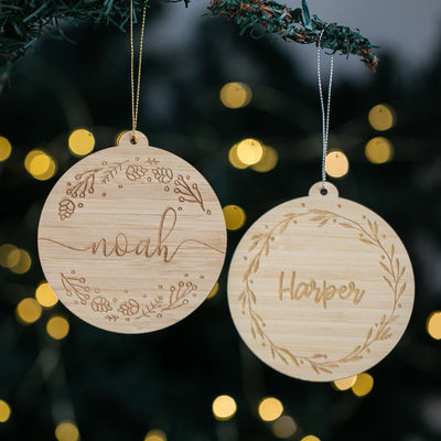 Two wooden Christmas ornaments with engraved names against a blurred festive background