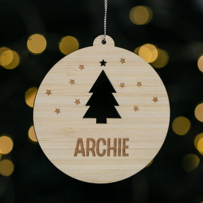 Wooden ornament with a Christmas tree design and 'ARCHIE' text, against a blurred light background.