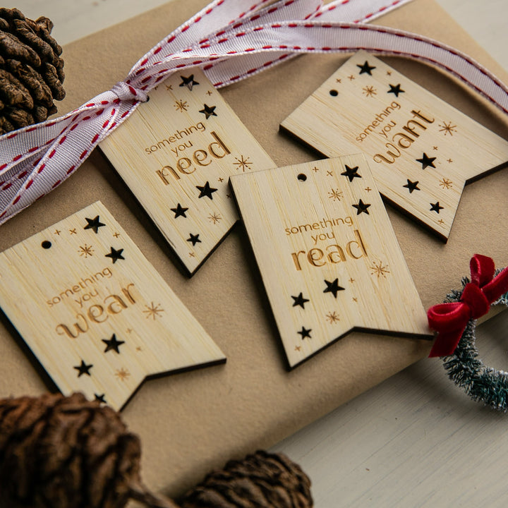 A wrapped gift with a red and white ribbon, decorated with Twinkle Twinkle Want, Need, Wear, Read Tags (Unpersonalised). Pinecones add a festive touch.