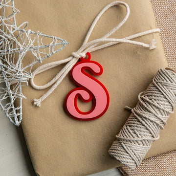 A wrapped gift with a white string bow, decorated with a red Personalised Deluxe Letter Gift Tag and a silver wire star, sits beside a roll of twine on a textured surface.
