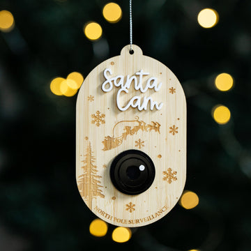 The Santa Surveillance Christmas Bauble is a bamboo camera-shaped ornament with "Santa Cam" and "North Pole Surveillance," decorated with Santa’s sleigh and snowflakes, adding festive charm to your Christmas tree.