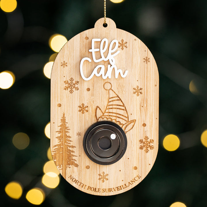 The Santa Surveillance Christmas Bauble features "Elf Cam" and "North Pole Surveillance," a faux camera lens, snowflakes, pine trees, and an elf hat—making it a unique ornament for your festive Christmas décor.