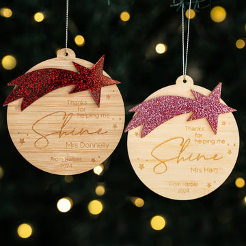 Two Shining Star Teacher Christmas Baubles with glittery shooting stars and "Thanks for helping me shine" engraved, personalized for Mrs Donnelly and Mrs Haig, hang on strings against a blurred, festive background.