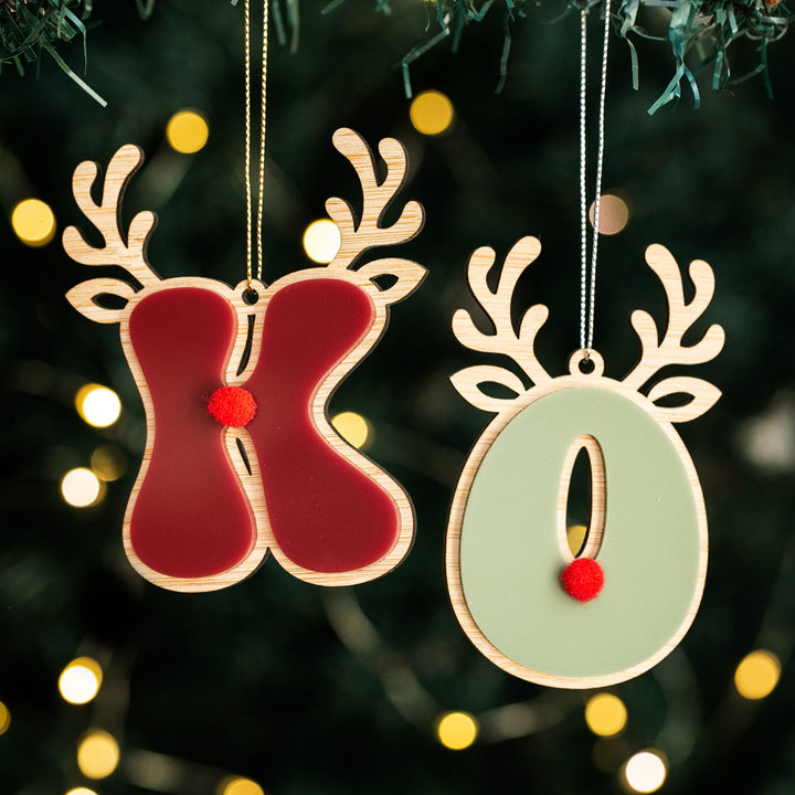 Two Christmas ornaments featuring Rudolph the reindeer with a red nose and antlers, hanging from a tree with festive lights.