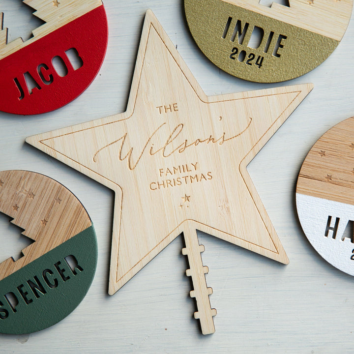 The Personalised Christmas Tree Topper is a wooden engraved star that reads "The Wilsons Family Christmas," surrounded by custom wooden ornaments named Jacob, Indie 2024, Spencer, and Harper.