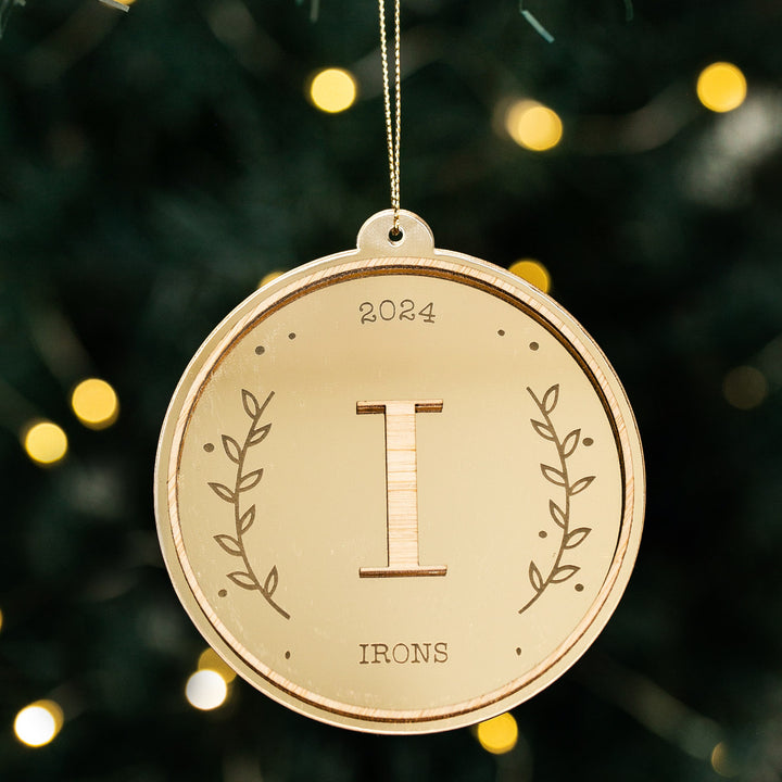 The Monogram Christmas Bauble is a round wooden ornament engraved with "2024," a large "I," "IRONS," and laurel branch designs—perfect as a unique personalised Christmas decoration.
