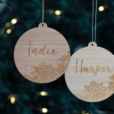 Two wooden ornaments with engraved names against a blurred Christmas tree background