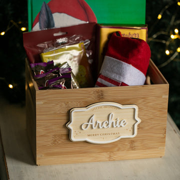 The Personalised Christmas Eve Box, labeled “Archie Merry Christmas,” comes filled with snacks, a Santa hat, and treats. Warm fairy lights create a festive atmosphere, making it a perfect Christmas keepsake.