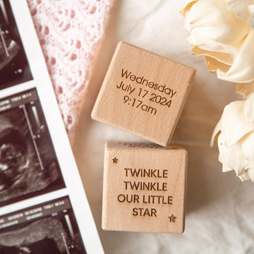 Two Personalised Wooden Blocks lay on a soft surface near dried flowers and ultrasound photos—an engraved baby keepsake and unique newborn gift, featuring "TWINKLE TWINKLE OUR LITTLE STAR" and birth details from July 17, 2024, 9:17am.