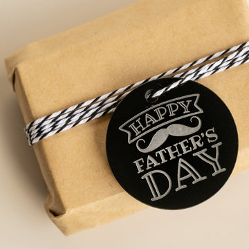A small gift wrapped in brown paper, tied with black-and-white twine, features the Father&