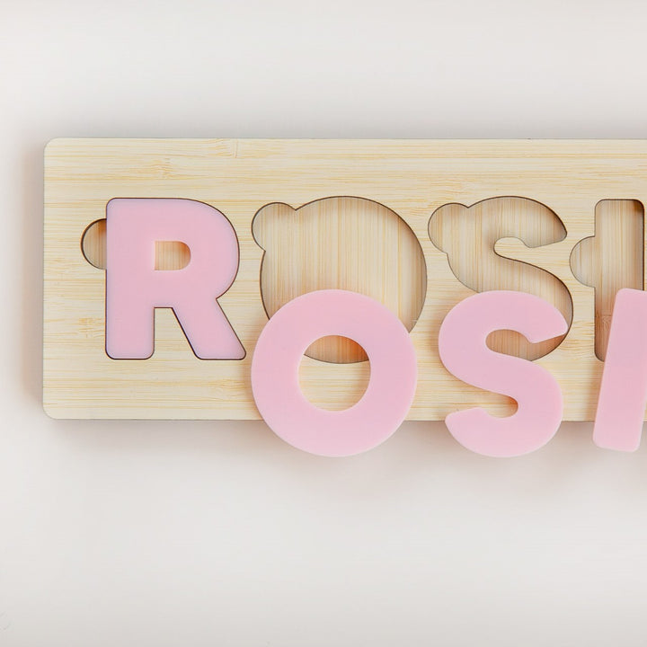 Personalised Name Puzzles: An adorable eco-friendly bamboo puzzle board with pastel pink letters spelling ROS—features the letter R fitted in its slot and the others on top. Perfect custom baby gift.