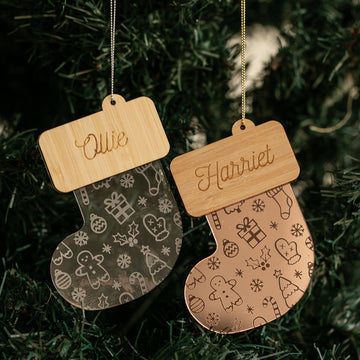 Two Christmas Stocking Baubles with holiday-themed engravings hang on a tree, each personalised with names like Ollie and Harriet. These festive ornaments make perfect custom decorations for your Christmas celebrations.