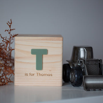 A Personalised Wooden Money Box sits on a white surface next to a toy metal truck, a keepsake gift ideal for little ones, and a small dried plant.