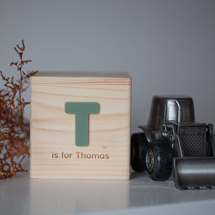 A Personalised Wooden Money Box sits on a white surface next to a toy metal truck, a keepsake gift ideal for little ones, and a small dried plant.