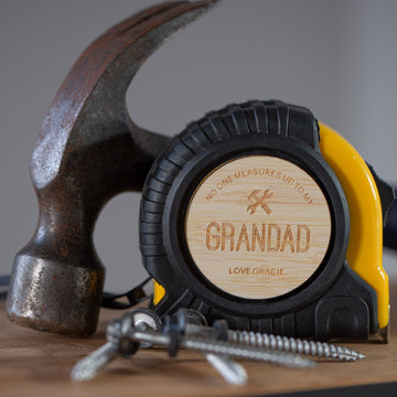 A close-up of a Personalised Tape Measure engraved with “No one measures up to my Grandad. Love Gracie,” shown beside a rusty hammer and screws—a unique Father’s Day gift and custom toolbox essential.