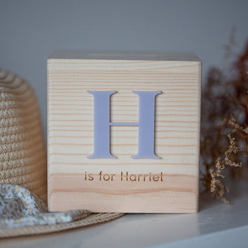 The Personalised Wooden Money Box features a large letter H and custom-engraved "is for Harriet" text on the front, making it a charming keepsake gift. Ideal for display, it adds a personal touch to any room.
