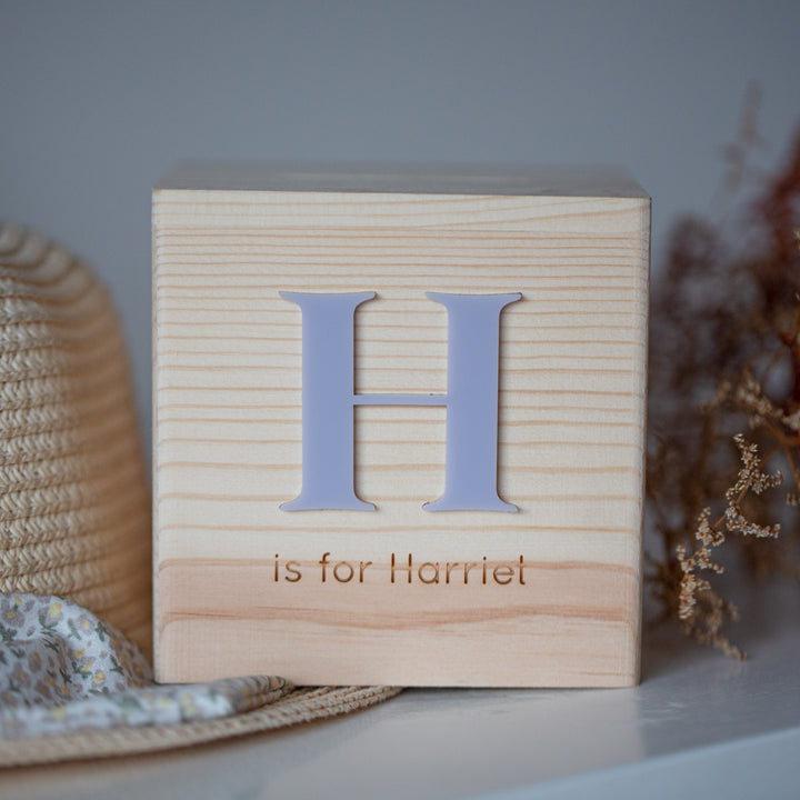 The Personalised Wooden Money Box features a large letter H and custom-engraved "is for Harriet" text on the front, making it a charming keepsake gift. Ideal for display, it adds a personal touch to any room.
