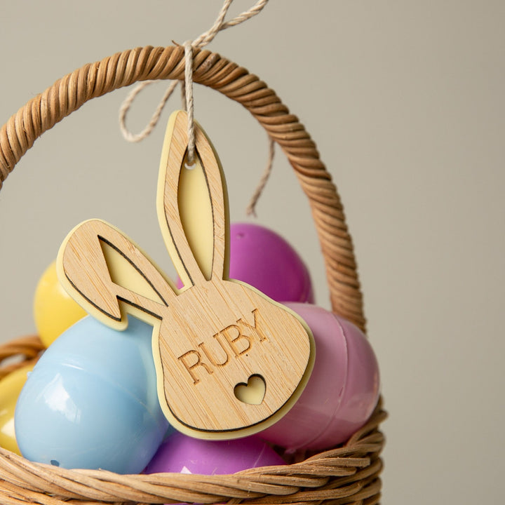 A wicker basket with pastel eggs features a Personalised Bunny Tales Easter Tag, engraved with the name RUBY and a small heart cutout on the handle—an ideal addition to your Easter collection.