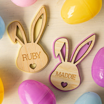 Two Personalised Bunny Tales Easter Tags, labeled RUBY and MADDIE, feature heart cutouts near the bottom and are displayed on a light surface with colorful plastic Easter eggs.
